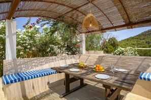 An outdoor dining area with a table set for four, surrounded by cushioned benches. - Peaceful Cala Vadella Villa with Pool (Sant Josep de sa Talaia)
