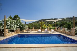 A swimming pool with lounge chairs and a shaded area, surrounded by stone walls and greenery. - Peaceful Cala Vadella Villa with Pool (Sant Josep de sa Talaia)