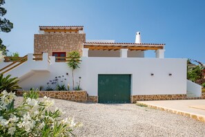 A modern house with a stone facade, a green door, and a gravel driveway. - Peaceful Cala Vadella Villa with Pool (Sant Josep de sa Talaia)