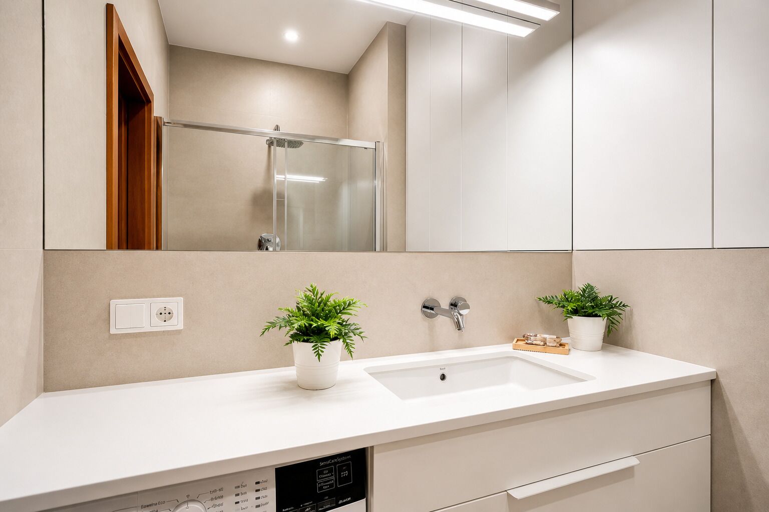 A modern bathroom with a white sink, two potted plants, a mirror, and a shower.