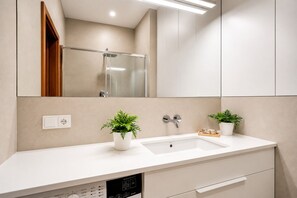 A modern bathroom with a white sink, two potted plants, a mirror, and a shower. - Kalina Apartment Old Town Gdańsk (Gdańsk)