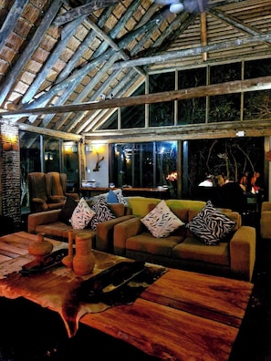 Un intérieur avec un plafond en bois, un canapé agrémenté de coussins à motifs et une table sur laquelle est posé un vase.