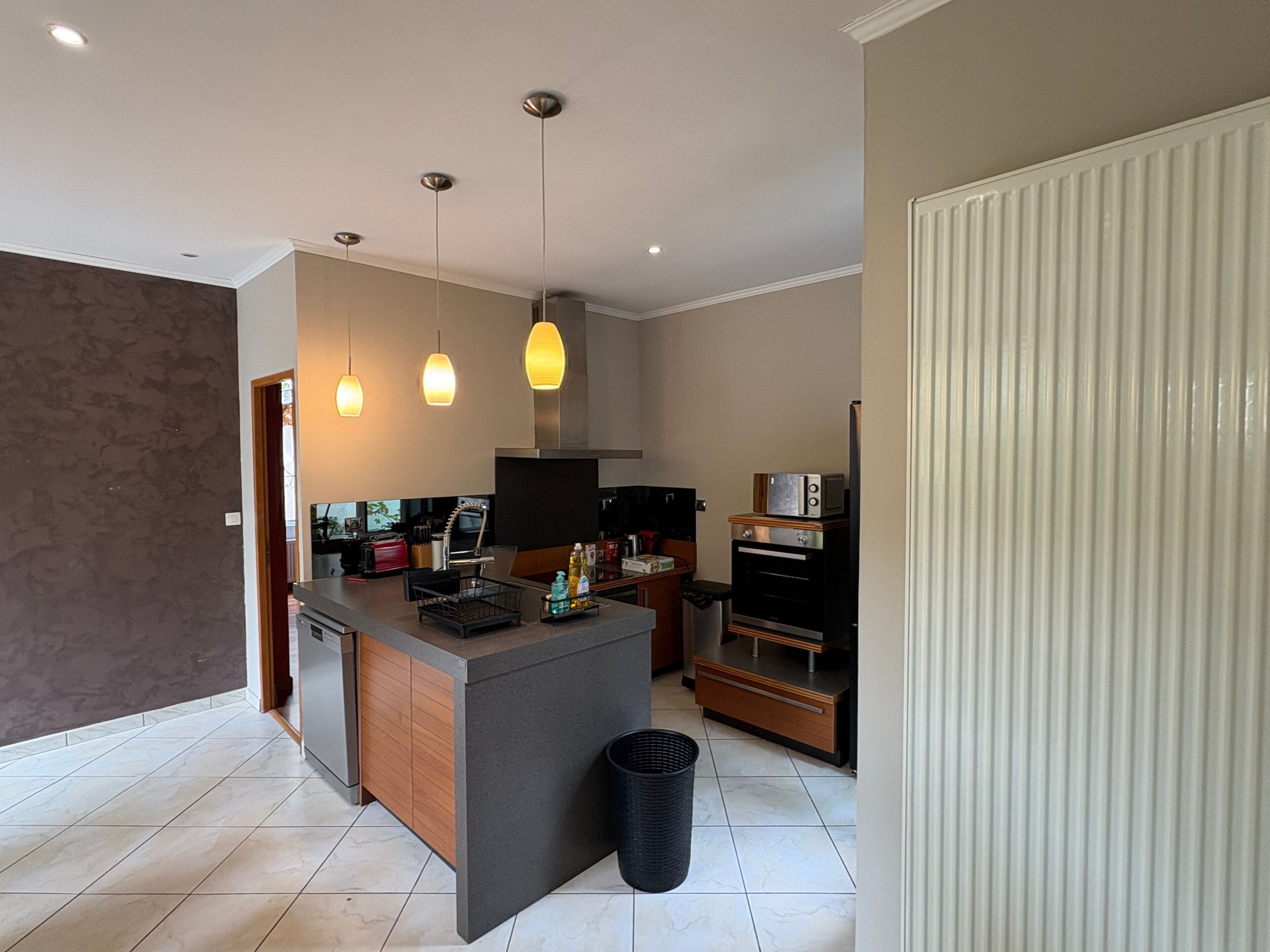 A modern kitchen with a central island, built-in oven, and pendant lighting.