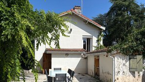 A white building with a tiled roof, a small patio with a table and chairs, and a wooden door. - Le Verger Secret – Mobility Lease at Lyon’s Doorstep, Ideal for Business Stays (Rillieux-la-Pape)