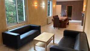 A modern living room with a sofa, a coffee table, and a dining area with chairs and a table. - Le Verger Secret – Mobility Lease at Lyon’s Doorstep, Ideal for Business Stays (Rillieux-la-Pape)