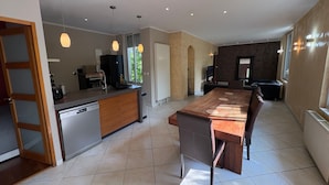 A modern kitchen with a central island, dining area with a long table and chairs, and a living area with a fireplace. - Le Verger Secret – Mobility Lease at Lyon’s Doorstep, Ideal for Business Stays (Rillieux-la-Pape)