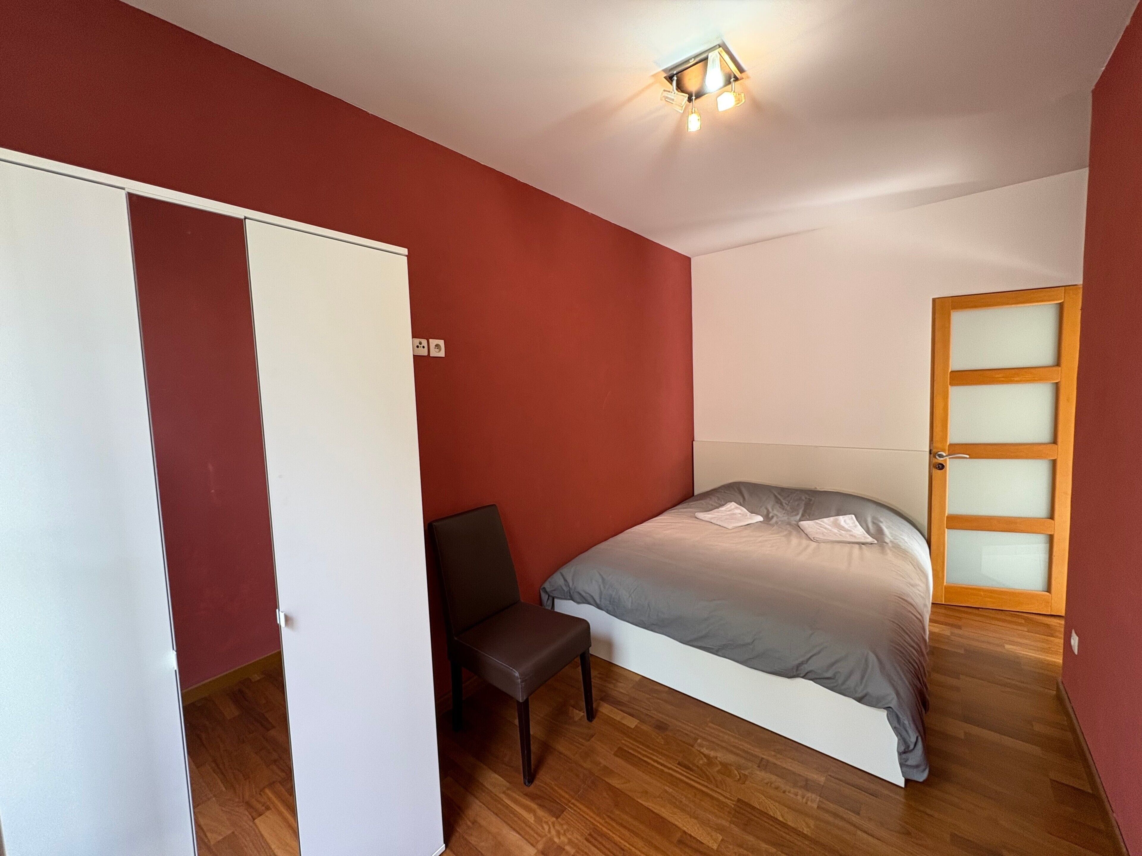 A bedroom with a bed, a chair, a wardrobe, and a door.