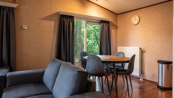 Quarto com sofá, mesa de jantar com cadeiras, relógio na parede e janela com cortinas.