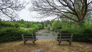 Een park met twee houten bankjes gericht op een poort, omringd door weelderige begroeiing.