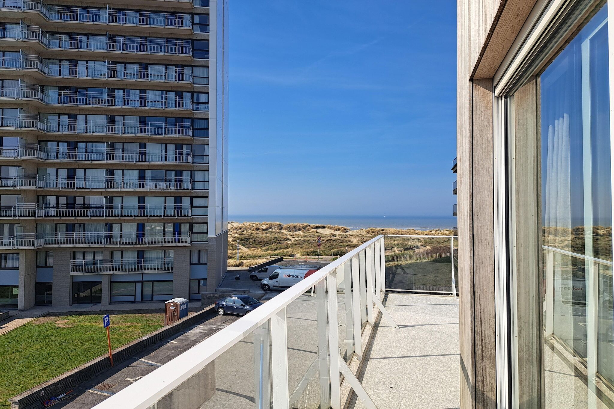 Ein Hochhaus mit mehreren Balkonen, einem Parkplatz und Blick auf den Strand.