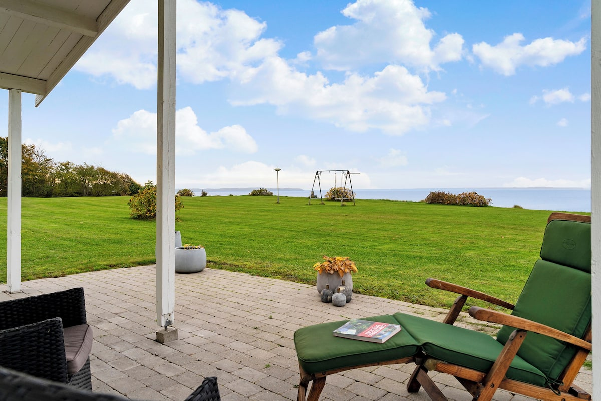 A patio with a swing set, green lawn, and a view of the sea.