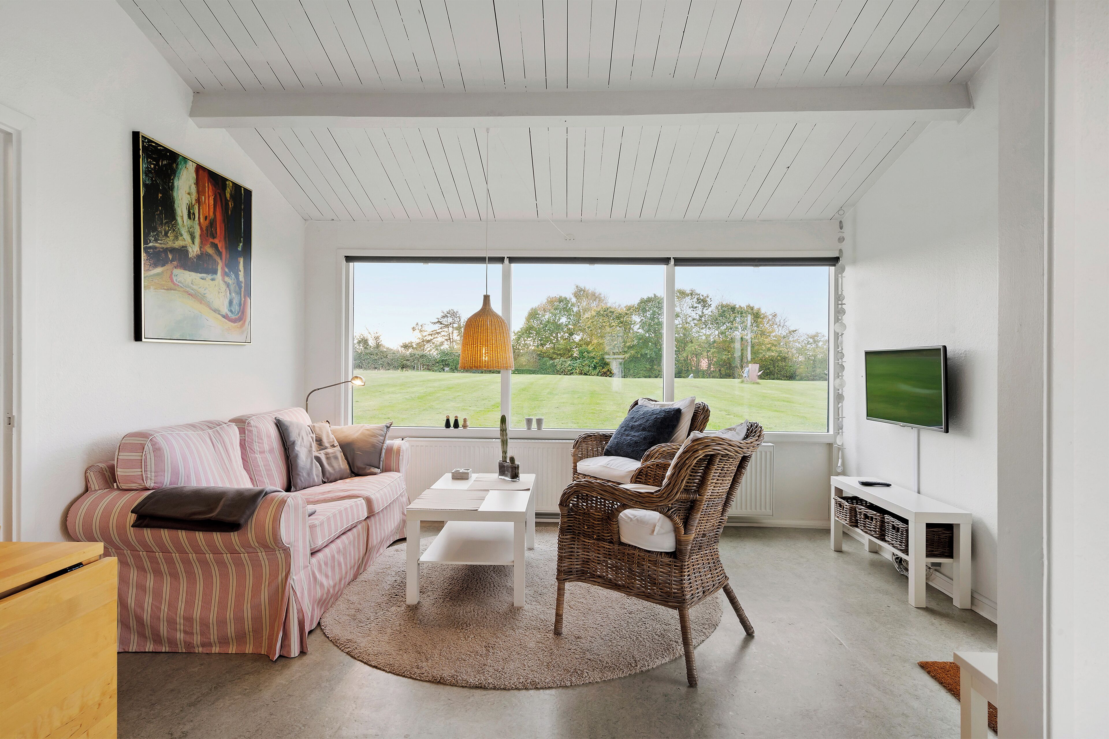 A modern living room with a large window, a television, and a wicker chair.