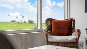A wicker chair with a brown cushion by a window overlooking a grassy field. - Sct. Knudsborg - Cottages (Middelfart)