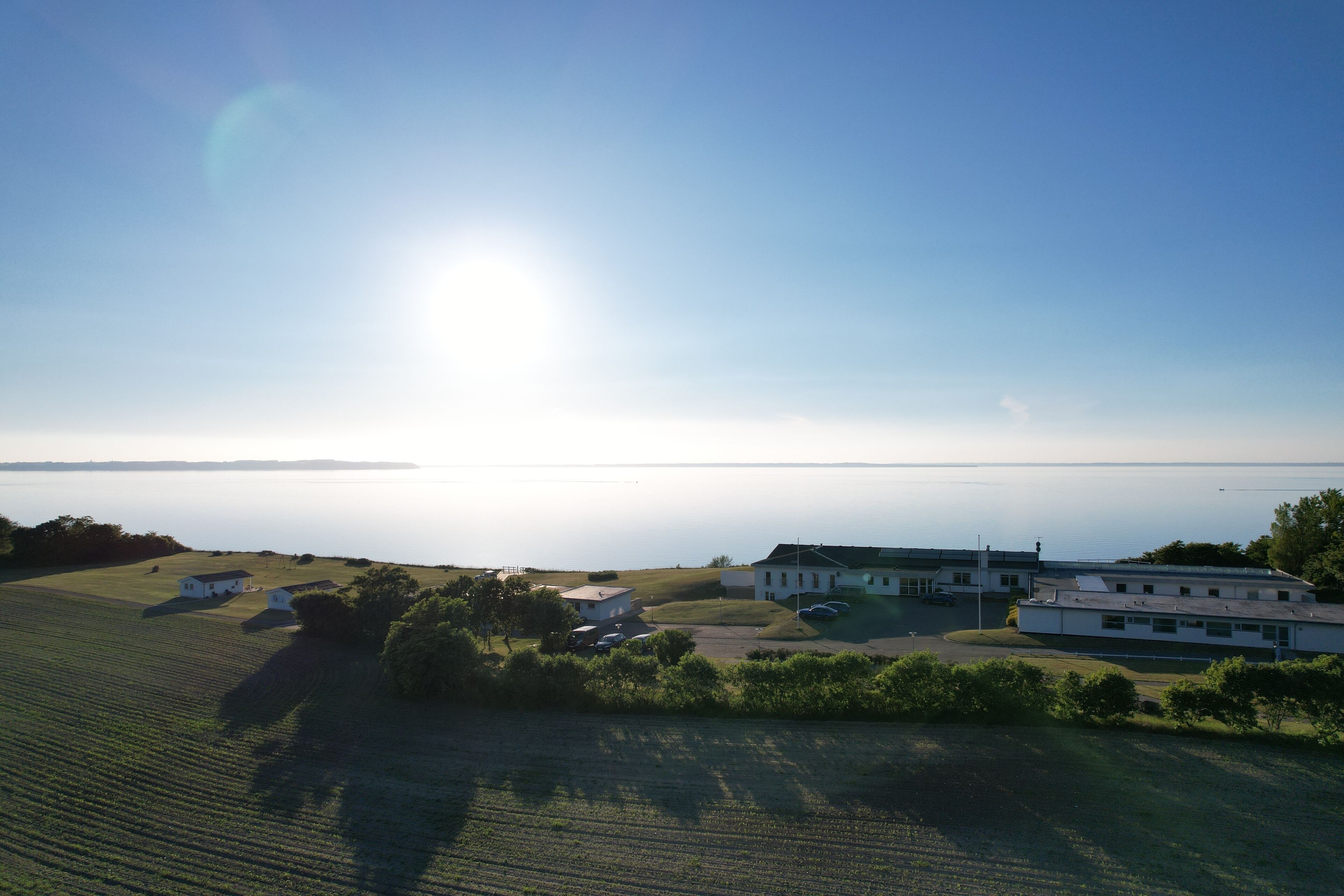 A coastal property with a large building, open fields, and a view of the sea.