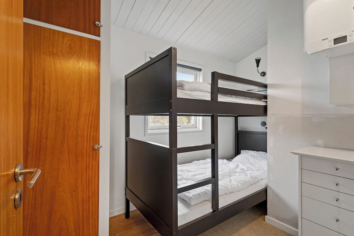 A bunk bed room with a wooden door, a white dresser, and a window.