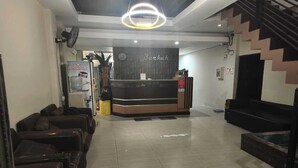 A hotel lobby with a reception desk, sofas, a staircase, and a water dispenser.