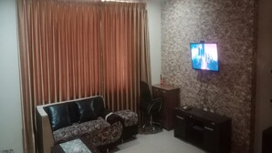 A living room with a sofa, a TV mounted on a textured wall, a desk, and a curtain.