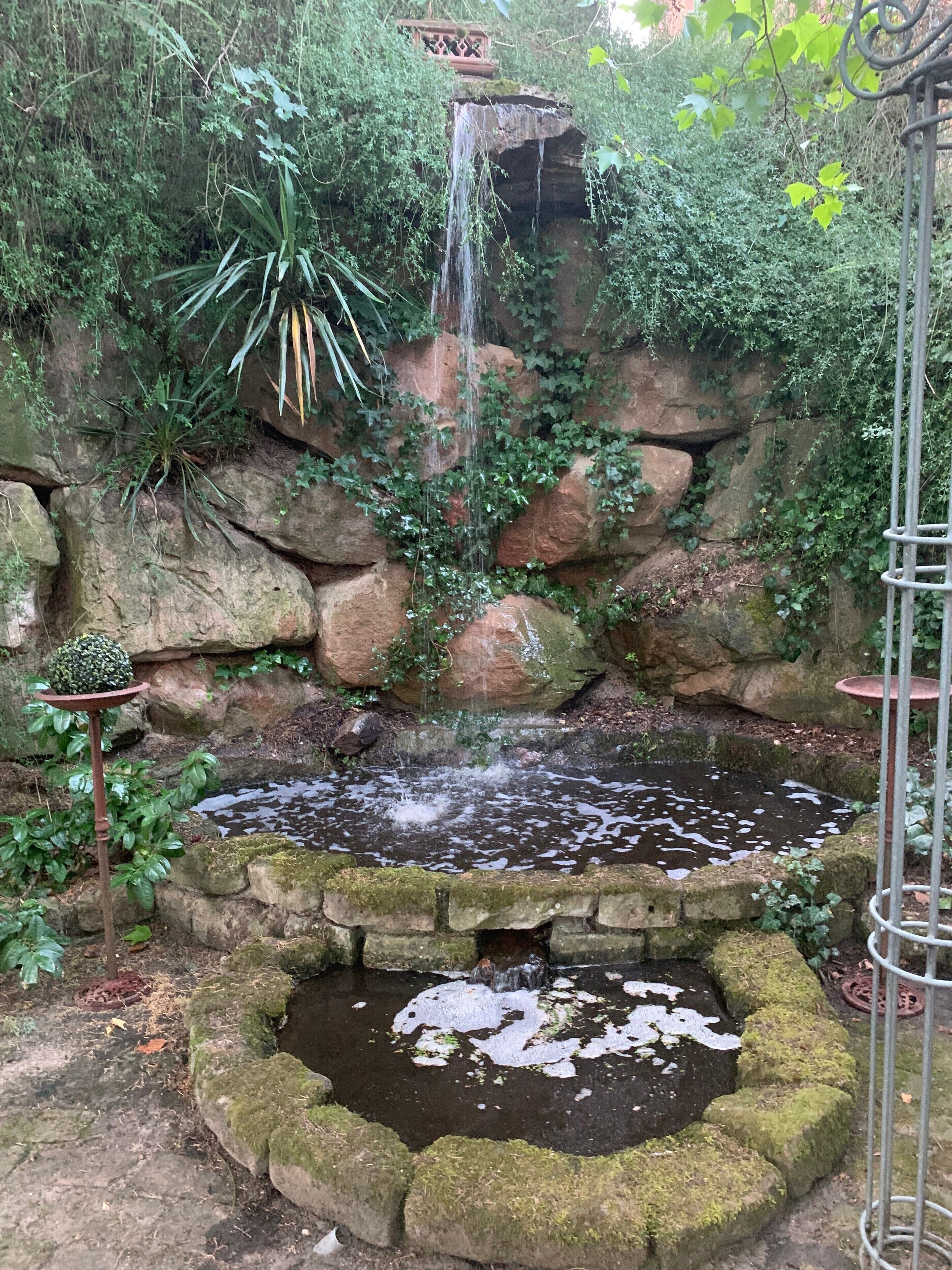Um jardim com uma pequena cascata, um lago e um muro de pedra rústica.
