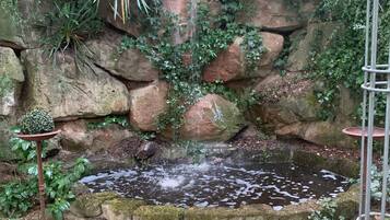 Um jardim com uma pequena cascata, um lago e um muro de pedra rústica.