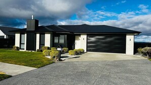 A modern two-story house with a garage, a well-maintained lawn, and a clear sky. - Private Luxury on Blue Dun (Taupō)