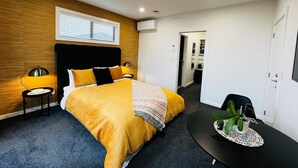 A modern hotel room with a bed, bedside lamps, a small table with a plant, and a door leading to a bathroom. - Private Luxury on Blue Dun (Taupō)