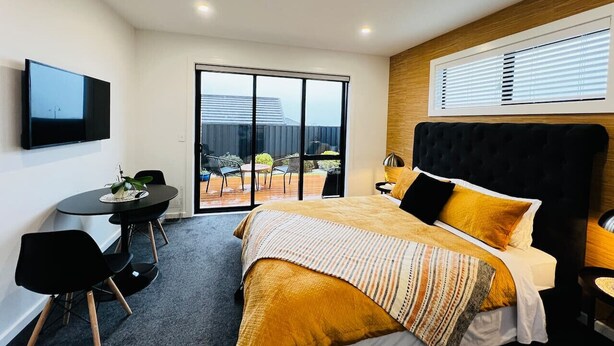 A modern hotel room with a bed, a desk, a TV, and a balcony with a view. - Private Luxury on Blue Dun (Taupō)
