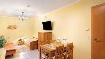 A room with a bed, a dining table with chairs, a TV mounted on the wall, and a door.