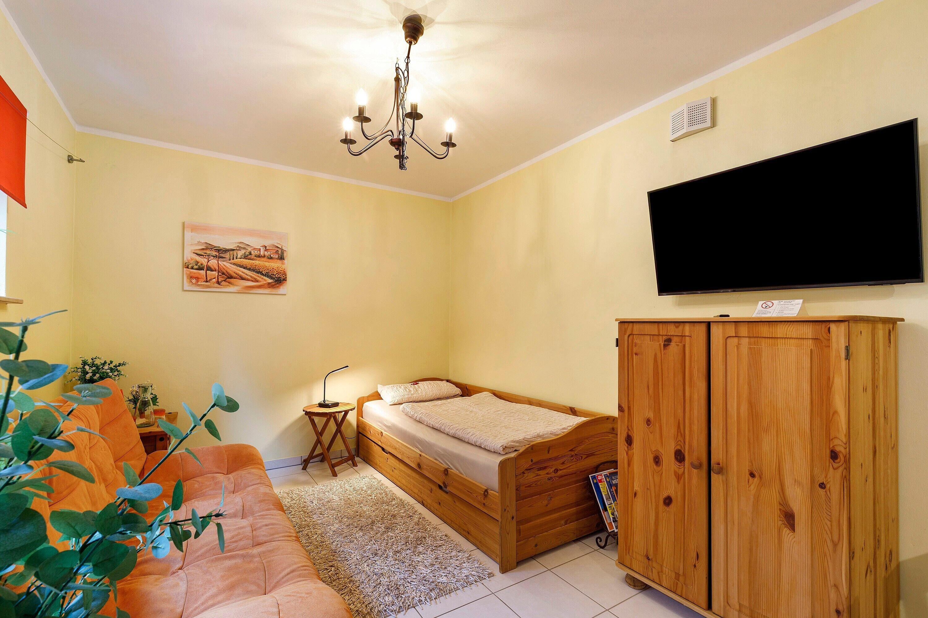 A bedroom with a bed, a television, a wooden cabinet, and a painting on the wall.