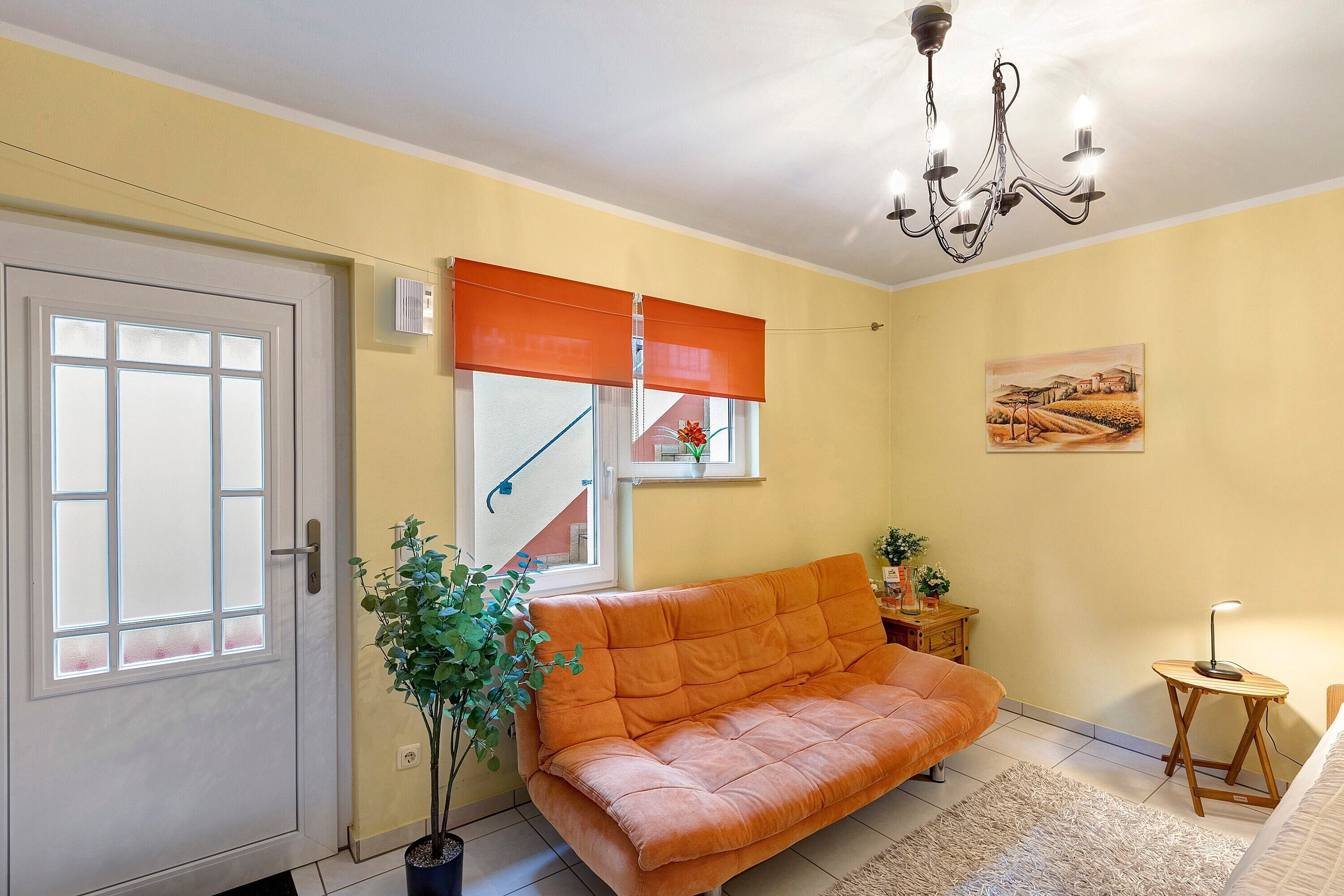 A room with a sofa, a potted plant, a small table with a lamp, a painting on the wall, and a door with frosted glass panels.
