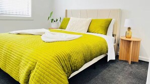 Un letto con copriletto verde trapuntato, un cuscino bianco e un comodino in legno con una lampada e una decorazione a forma di ananas.