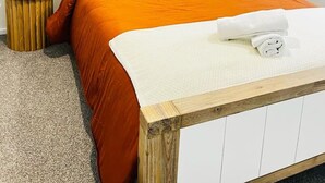 Una cama bien hecha con una colcha naranja, dos lámparas de noche y un cabecero de madera.
