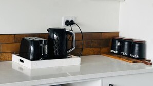 Una cocina con cafetera, tostadora y recipientes etiquetados con café, té y azúcar.