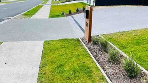 Un edificio moderno con garaje, entrada para vehículos y zona verde con un cartel.