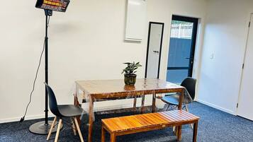 A room with a table, chairs, a bench, a standing heater, a potted plant, and a door.