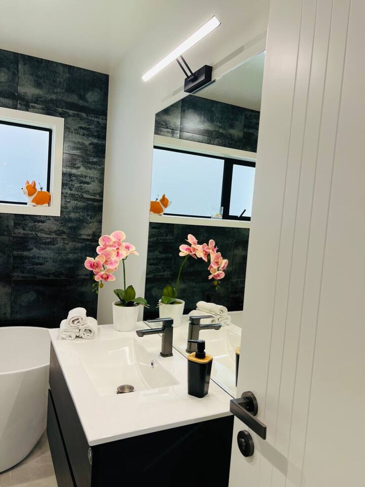 Un bagno moderno con un lavandino bianco, due rubinetti, uno specchio e una finestra vista.