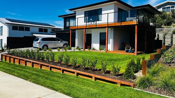 A modern two-story house with a carport, a well-maintained lawn, and a wooden deck.