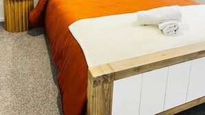 A neatly made bed with a wooden headboard, two bedside lamps, and a small round table with a lamp. - Penny Retreat with 1 Bedroom (Taupō)