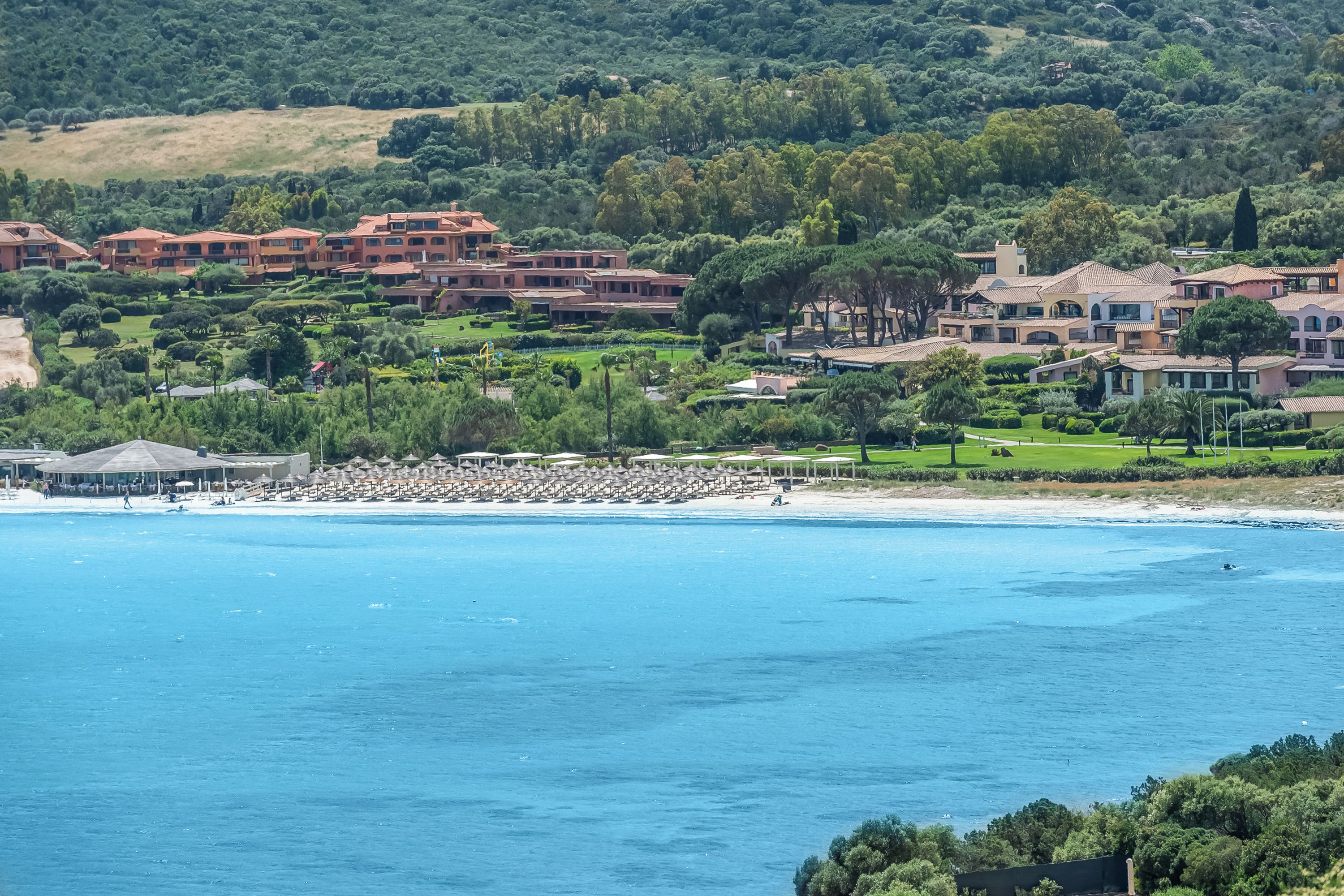 A coastal resort with multiple buildings, a beach, and lush greenery.