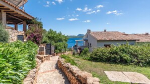 A stone pathway leading to a building with a balcony overlooking a coastal area. - Casa Titta (Olbia)