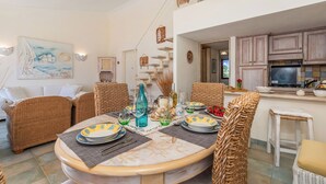 A dining area with wicker furniture, a table set for four, and a kitchen in the background. - Casa Titta (Olbia)