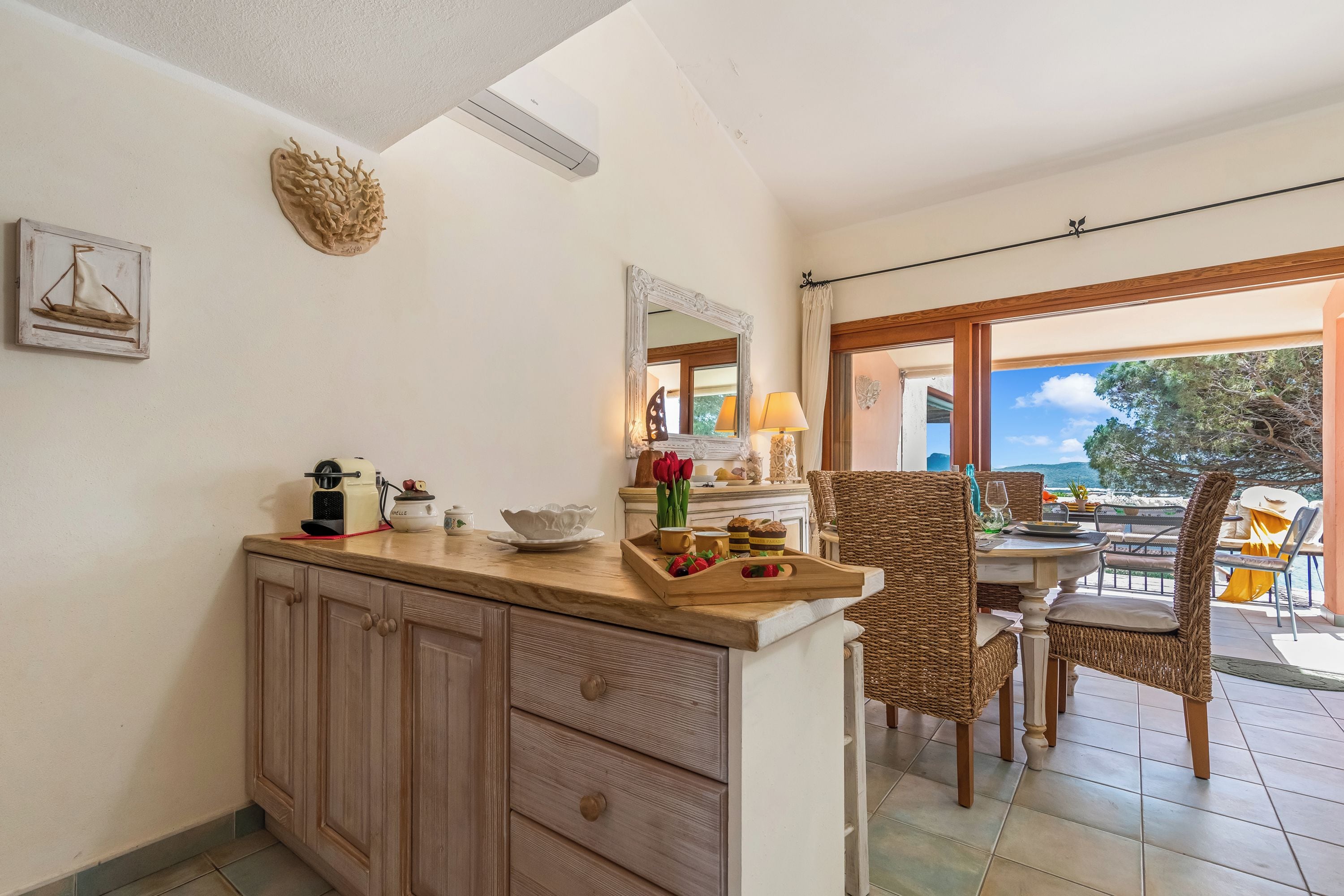 Une cuisine dotée d’un plan de travail en bois, de placards, d’un coin repas avec des chaises en osier, une table et une vue sur l’extérieur.