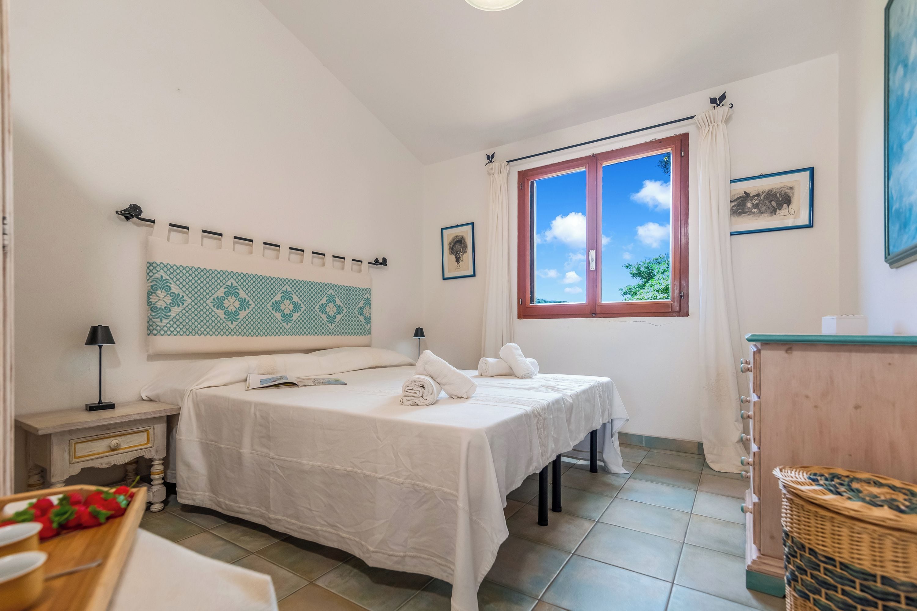 Une chambre à coucher avec un lit, des tables de chevet, une fenêtre avec des rideaux et un tableau accroché au mur.