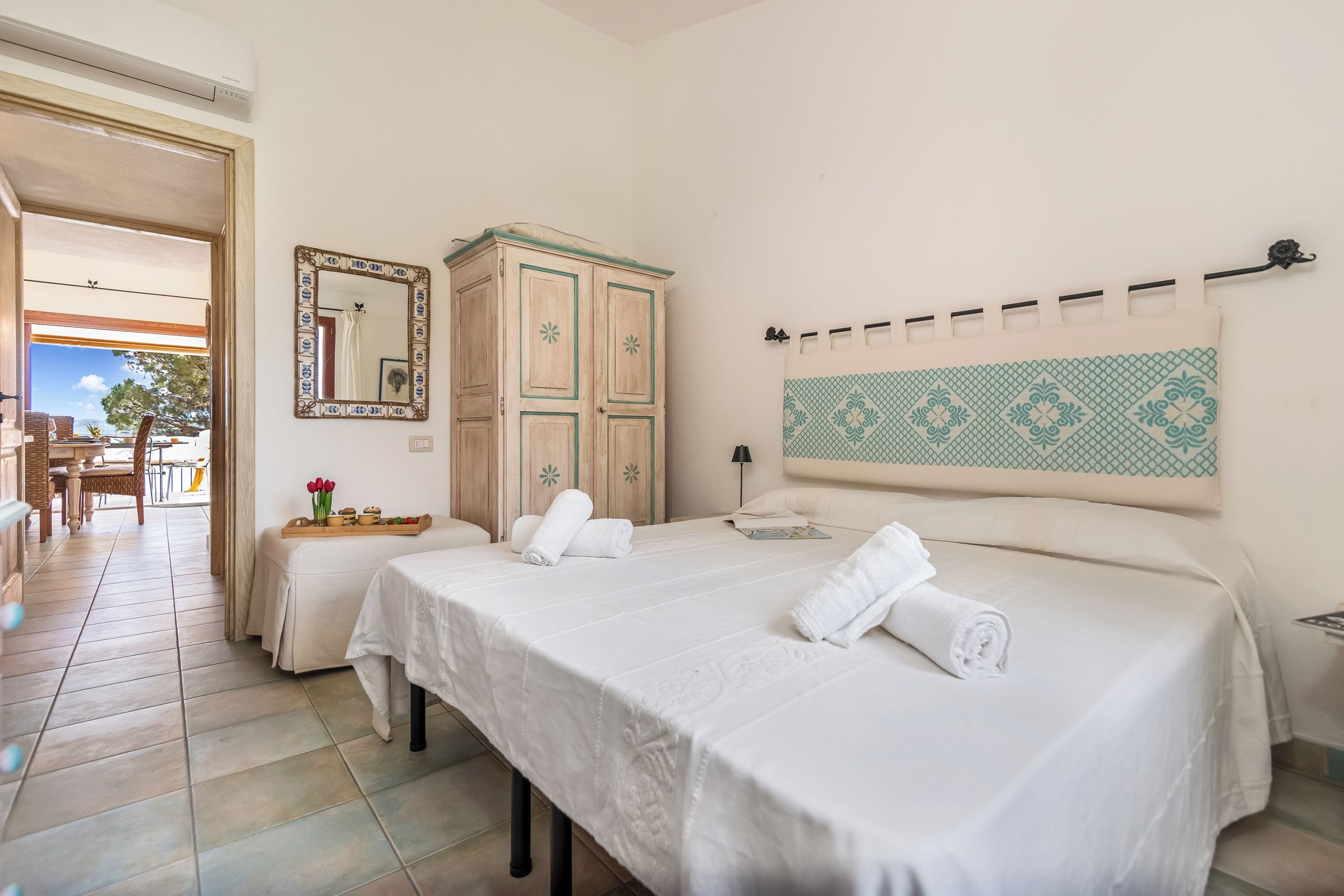 Une chambre d’hôtel avec deux lits, une armoire en bois, un miroir, une décoration murale à motifs et une vue sur l’extérieur.