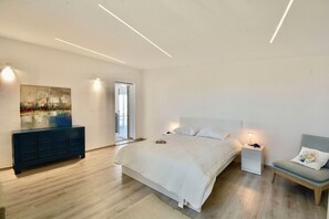 A modern bedroom with a large bed, bedside tables, a chair, a painting, and a sliding glass door leading to a balcony. - Rari House by Geco Vacation Rentals (Brucoli)
