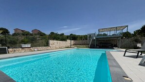A rectangular swimming pool with clear blue water, surrounded by a stone wall and a paved deck. - Rari House by Geco Vacation Rentals (Brucoli)