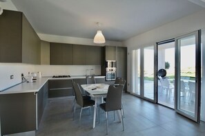 A modern kitchen with a dining area, large windows, and a view of the outdoors. - Rari House by Geco Vacation Rentals (Brucoli)