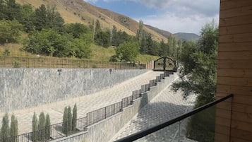 A balcony with a view of a stone pathway leading to a bridge, surrounded by greenery and hills.