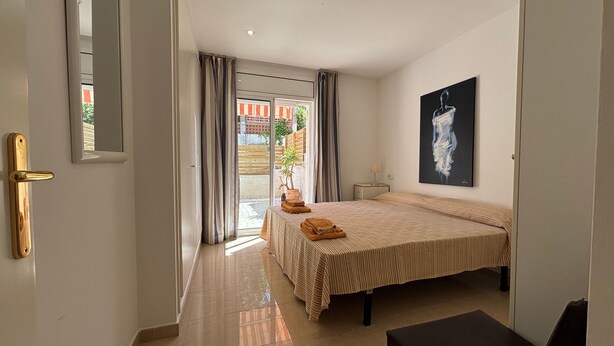 A hotel room with a bed, a nightstand, a painting, and a view through the door. - Apartment 'Brisas Del Mar Pb-3' with Shared Pool, Wi-Fi and Air Conditioning (Torroella de Montgrí)