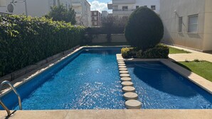 A swimming pool with a stone border, surrounded by greenery and buildings. - Apartment 'Brisas Del Mar Pb-3' with Shared Pool, Wi-Fi and Air Conditioning (Torroella de Montgrí)