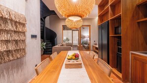 Un espace repas moderne avec une table en bois, des éléments de décoration murale en fibres tressées et un grand luminaire suspendu.